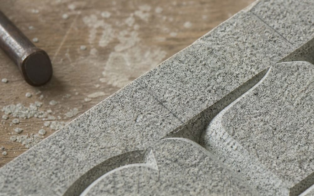 Meißel liegt neben frisch in Granit gehauenen Buchstaben